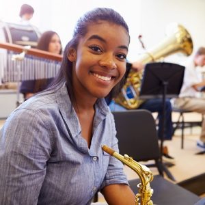 Smiling female high school pupil with saxophone