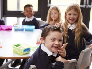 Elevated view of primary school kids sitting together at a round table to eat their packed lunches, some turning around to face the camera