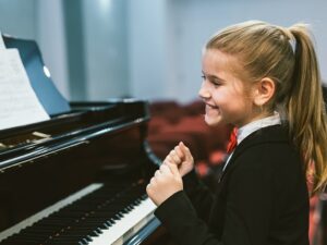 happy little girl teaching to play piano in music school