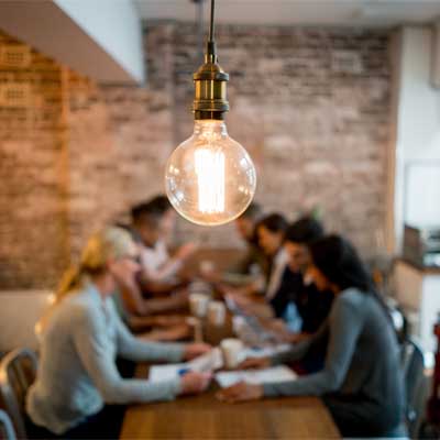 People sat round a table chatting, with a big lightbulb in the foreground