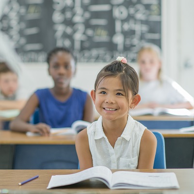 Image of a little girl smiling in class with a book in front of her. Symbolises the Services For Education SCITT course