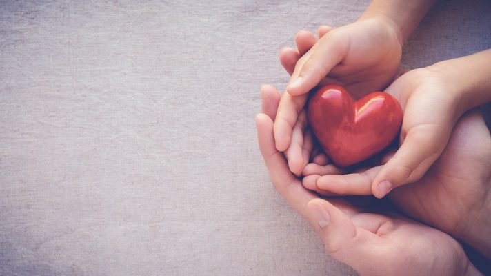 A picture of a child holding a heart and someone holding their hands