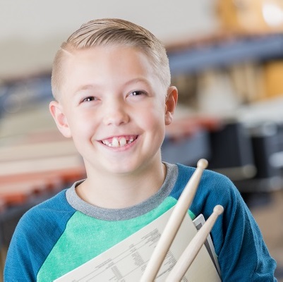 Picture of a boy smiling holding some drumsticks, symbolising The Music Cares Project