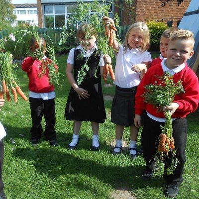 5 kids all holding up carrots they have grown. During a Health For Life session