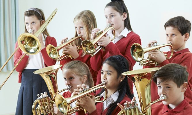 Group of children playing instruments in class in school uniform