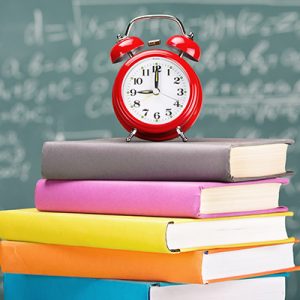 Stack of colourful books with an alarm clock on top and blackboard background