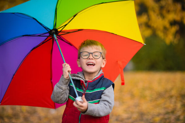 little boy smiling holding a rainbow coloured umbrella
