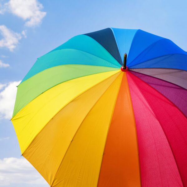 rainbow coloured umbrella in front of a blue sky with white clouds.