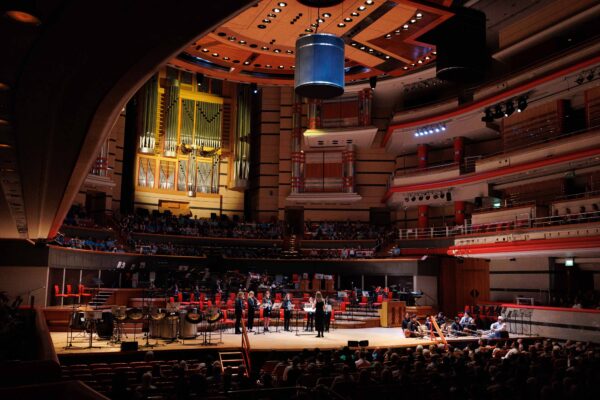 SFE Ensembles performing on stage at Symphony Hall in Birmingham, with musicians playing to a large seated audience inside the concert hall.
