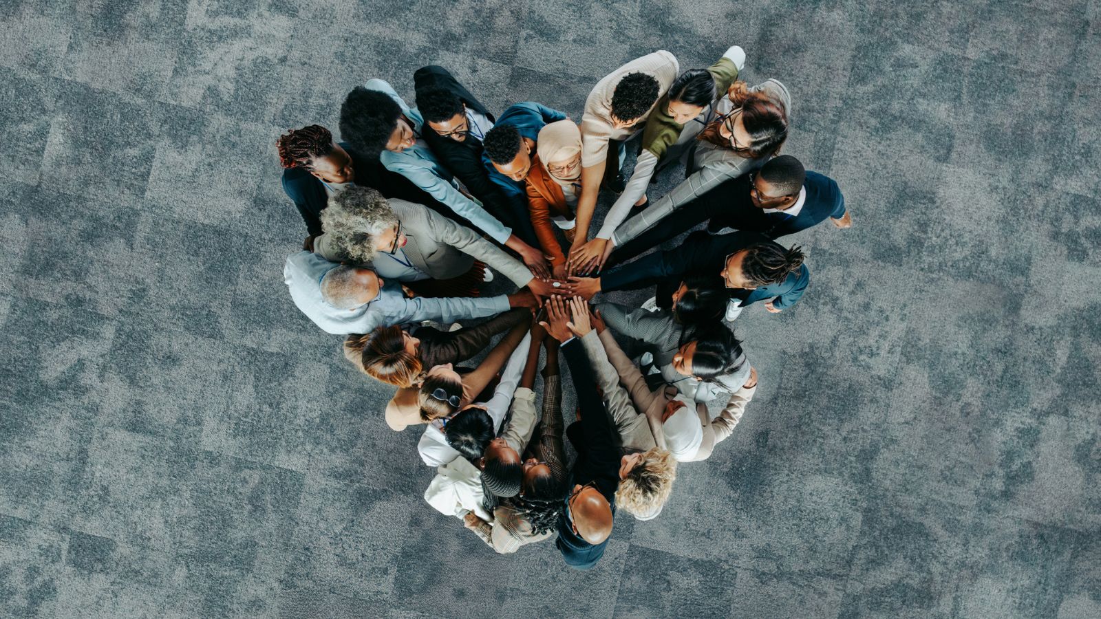 A diverse group of professionals standing in a circle from a top-down perspective, joining their hands together in the centre.